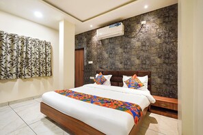 Un dormitorio con cama, mesita de noche, aire acondicionado de pared y cortina estampada.