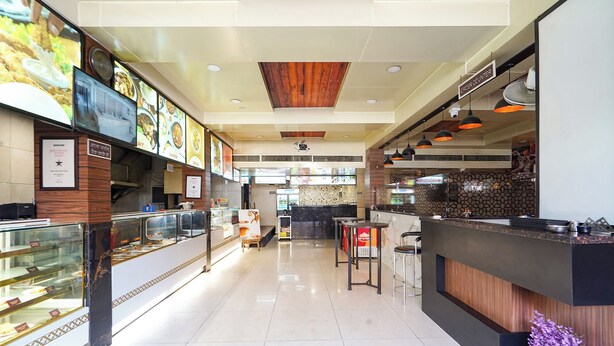 A clean, modern restaurant interior with a counter, display cases, and a wooden ceiling. - FabHotel Zamzam Residency (Bhopal)