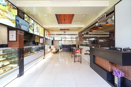 A clean, modern restaurant interior with a counter, display cases, and a wooden ceiling.. Fabhotel Zamzam Residency