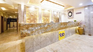 A hotel reception desk with a marble counter, a reception sign, a clock, and a reception sign on the wall. - FabHotel Zamzam Residency (Bhopal)