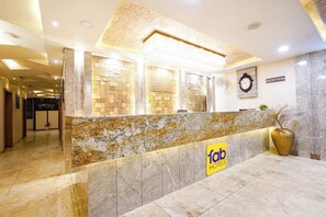 Un mostrador de recepción de hotel con encimera de mármol, un cartel de recepción, un reloj y una señalización en la pared.