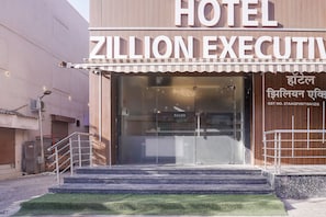 A hotel entrance with a sign reading 'ZILLION EXECUTIVE,' a staircase leading up to the entrance, and a small grassy area in front.