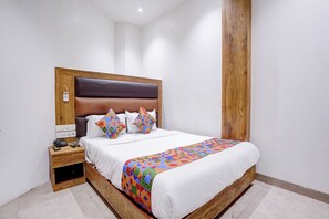A neatly made bed with a patterned bedspread, a wooden headboard, and a bedside table with a phone and charger. - Fabhotel Zillion Executive (Mumbai)