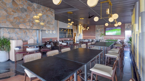 A spacious restaurant with multiple tables and chairs, a stone wall, and hanging pendant lights. - Fabhotel the prime Briklane -BTM Layout (Bangalore)