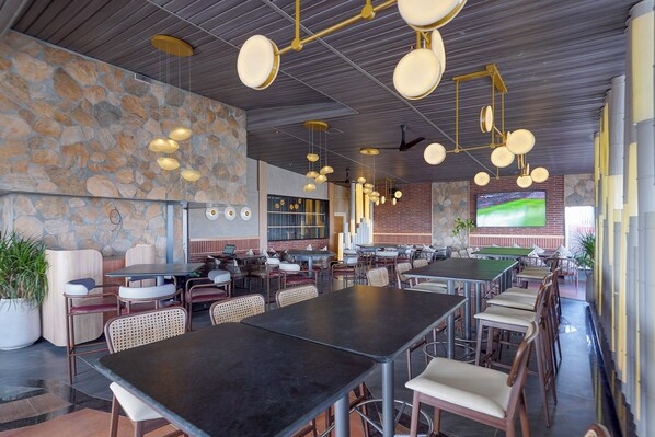 A spacious restaurant with multiple tables and chairs, a stone wall, and hanging pendant lights. - Oriva Briklane (Bangalore)