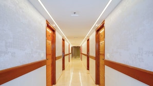 A hotel hallway with wooden doors, a tiled floor, and a ceiling light. - Fabhotel the prime Briklane -BTM Layout (Bangalore)