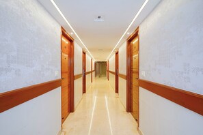 A hotel hallway with wooden doors, a tiled floor, and a ceiling light. - Oriva Briklane (Bangalore)