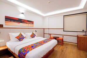 A hotel room with a bed, a desk, a chair, a painting, and a projector screen. - Oriva Briklane - BTM Layout (Bangalore)