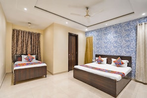 A hotel room with two wooden beds, a ceiling fan, and patterned wallpaper. - Via Amazing Guest House (New Delhi)