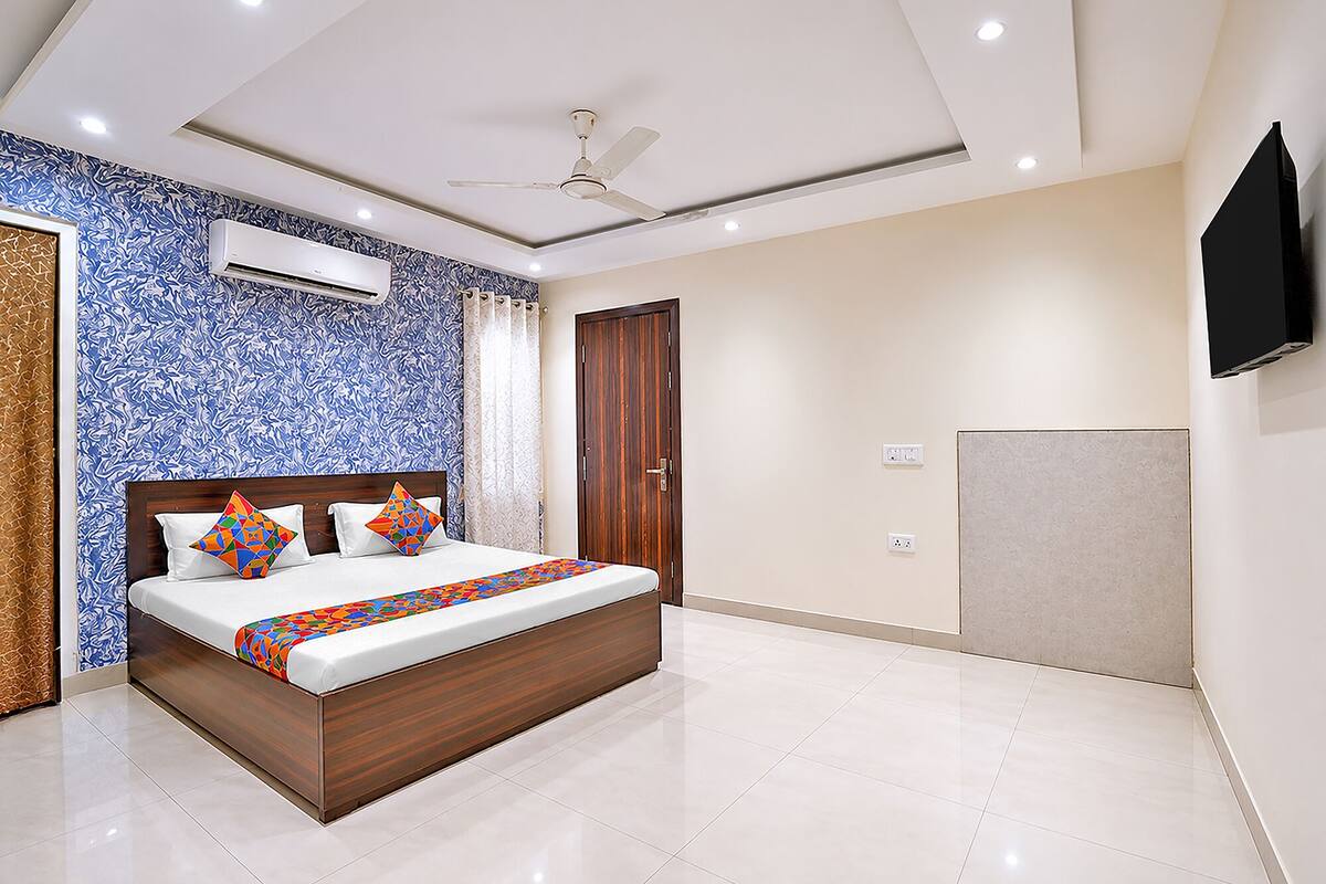 A bedroom with a bed, ceiling fan, air conditioning unit, and a TV mounted on the wall.