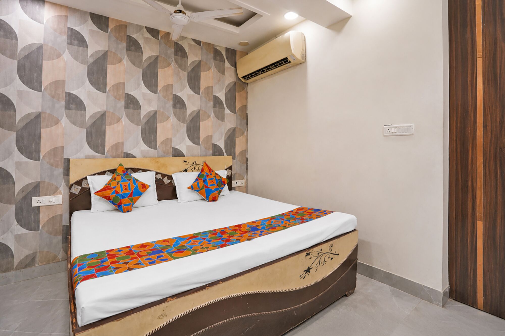 A bed with a patterned bedspread, a headboard with geometric designs, and a wall with circular patterns.