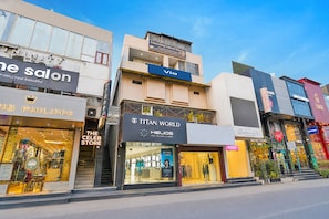 A row of commercial buildings with various storefronts, including a salon, a watch store, and a clothing store. - Via Amazing Guest House (New Delhi)