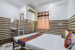 A hotel room with a bed, a bedside table, a mirror, a sink, and a window with a curtain.