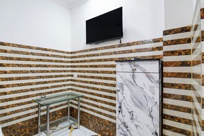 Casa de banho nos cantos, com uma mesa de vidro, um armário branco e uma televisão preta fixada na parede.