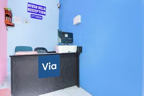 Um balcão de recepção com uma placa azul, um computador, um telefone e uma cadeira.