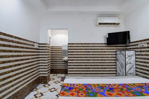 A bathroom with patterned walls, a tiled floor, a sink, a mirror, a television, and a marble cabinet. - Via Ayush Villa (Kolkata)