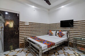 A small, compact room with a bed, a television mounted on the wall, and a patterned floor. - Via Ayush Villa (Kolkata)