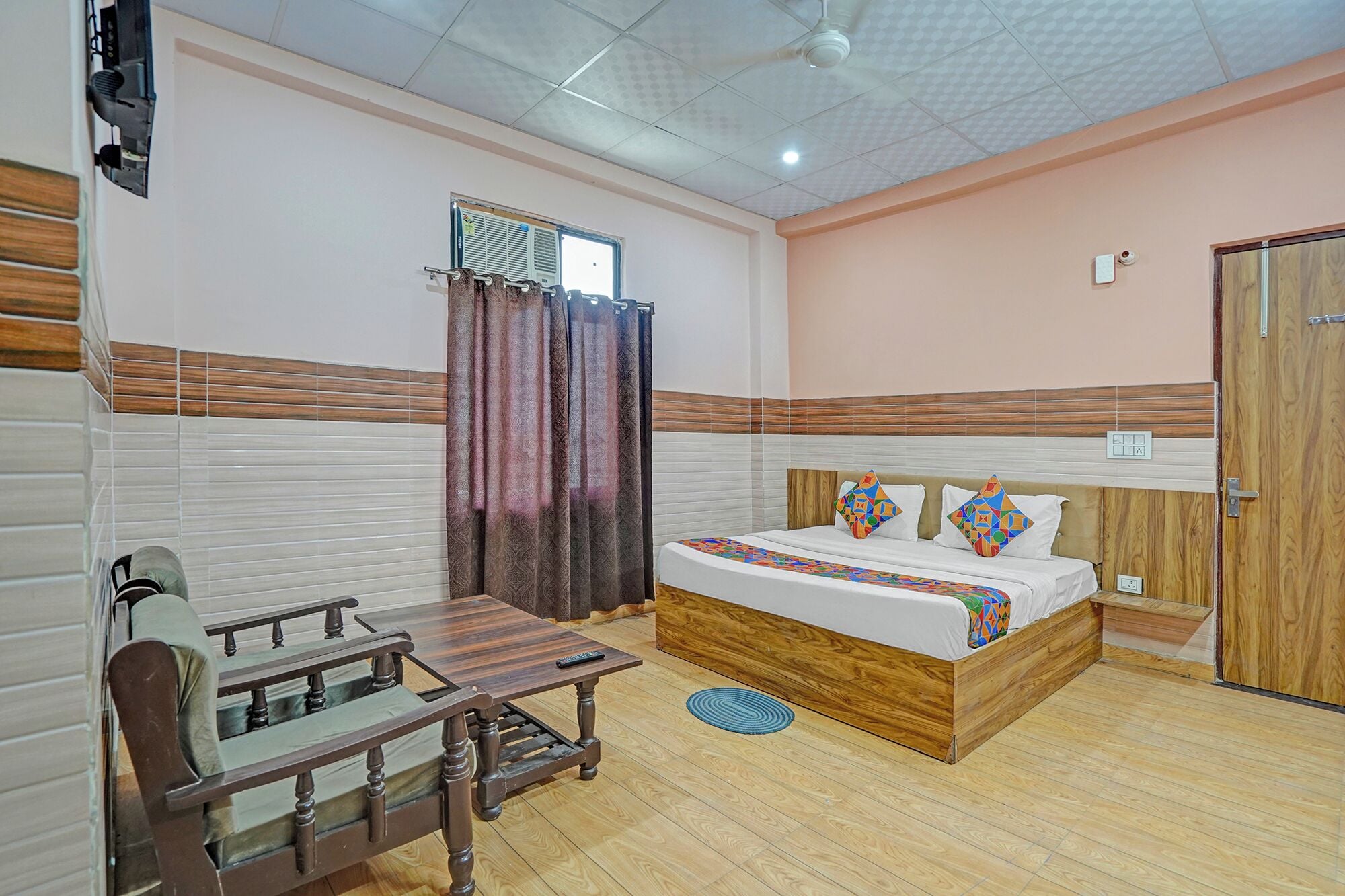Una habitación de hotel con cama, escritorio, ventana con cortinas, ventilador de techo y puerta.