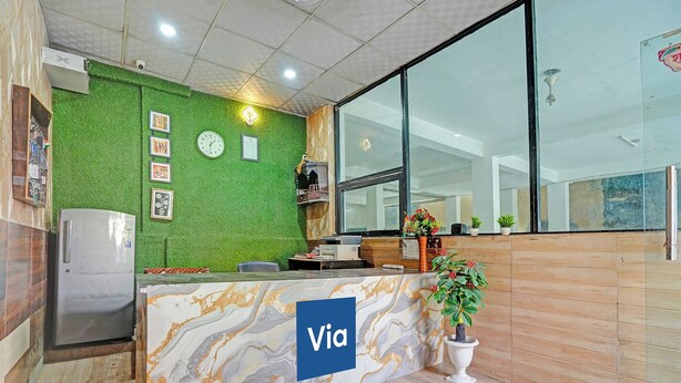 A reception area with a green wall, a clock, a refrigerator, and a marble counter with the word 'Via' on it. - Via Balram - Metro Station Sector 34 Noida (Noida)