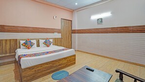 A hotel room with a bed, a bedside table, a wooden floor, a ceiling fan, and a wall-mounted light. - Via Balram - Metro Station Sector 34 Noida (Noida)
