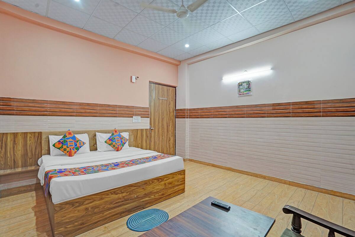 Habitación de hotel con cama, mesita de noche, piso de madera, ventilador de techo y lámpara fijada a la pared.