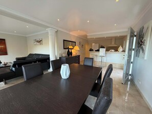 Ein modernes Wohnzimmer mit einem dunklen Holzes Esstisch, schwarzen Ledersofas und einer weißen Vasen-Mittelstück.