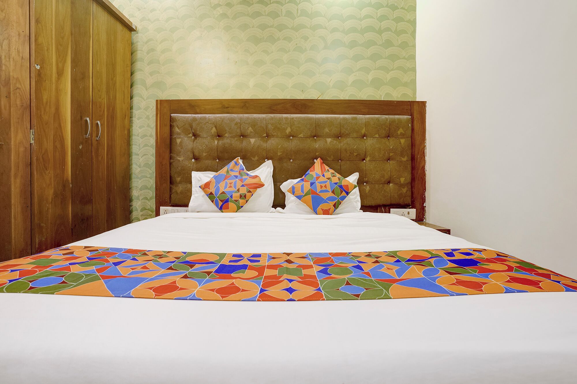 Una cama con colcha de estampado geométrico, cabecera capitonada y dos almohadas decorativas.