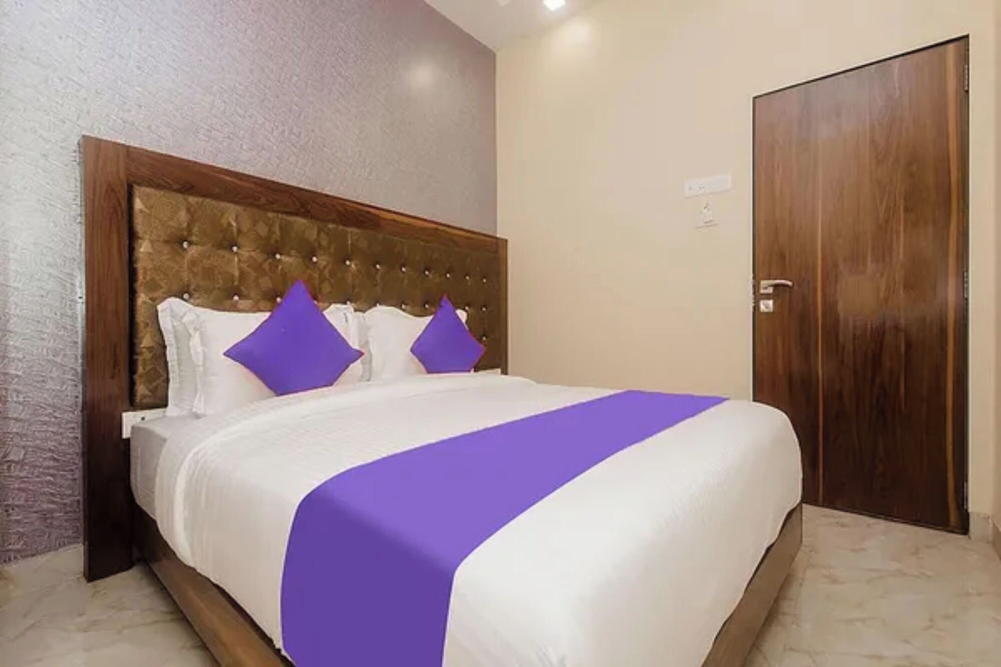 A hotel room with a large bed, a wooden headboard, and a closed door.