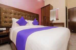 A hotel room with a large bed, a wooden headboard, a nightstand, a dresser, a mirror, and a door. - Via Green Forest (Mumbai)