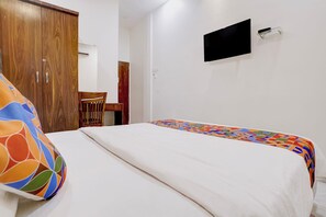 Un dormitorio con cama, un armario de madera, una silla y un televisor en la pared.