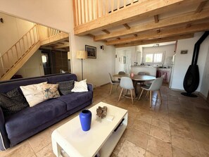 Ein Wohnzimmer mit Sofa, Couchtisch und Essbereich mit Stühlen. Im Hintergrund ist eine Treppe zu sehen.