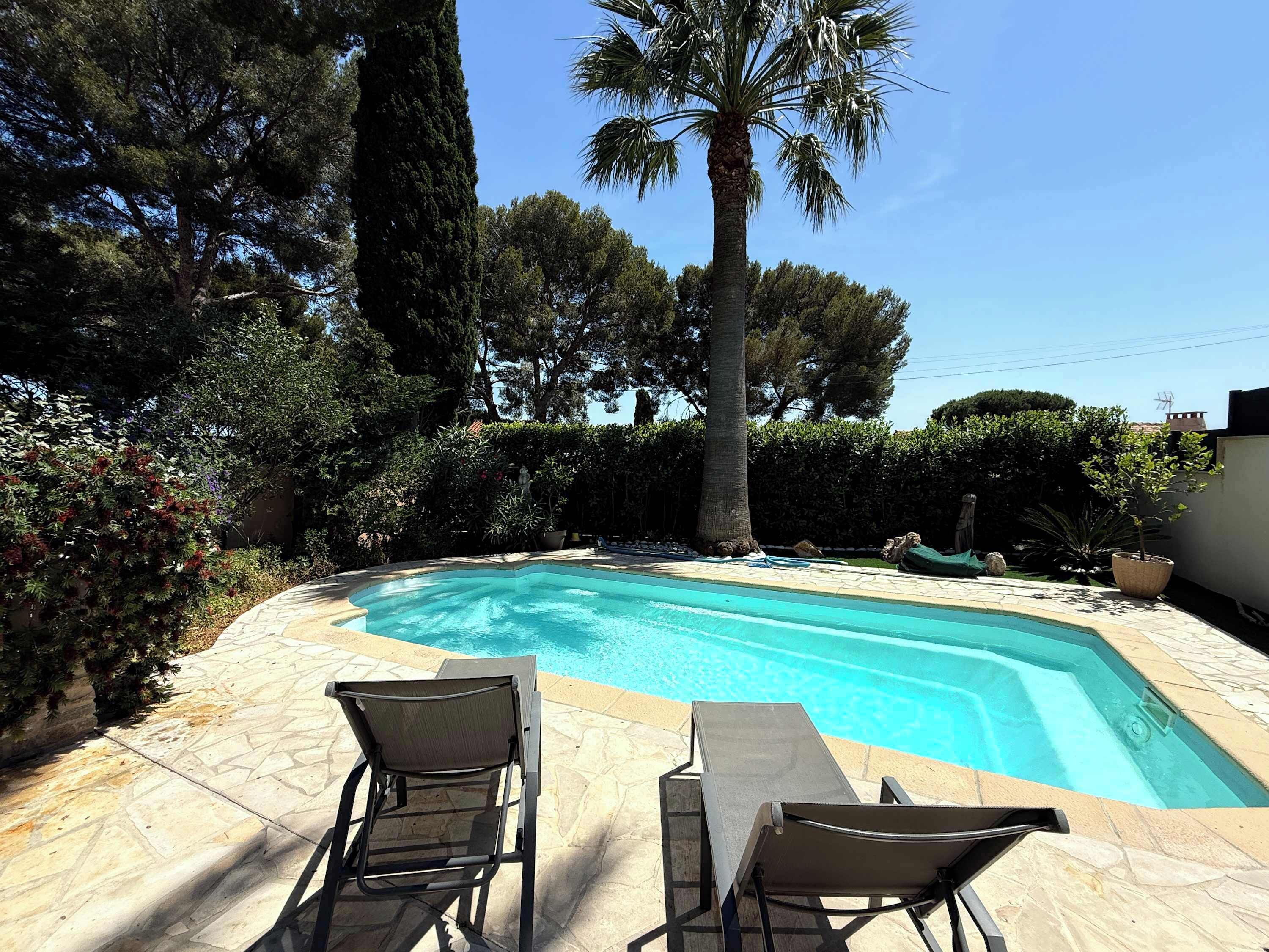 A swimming pool with two lounge chairs, surrounded by trees and a clear sky.