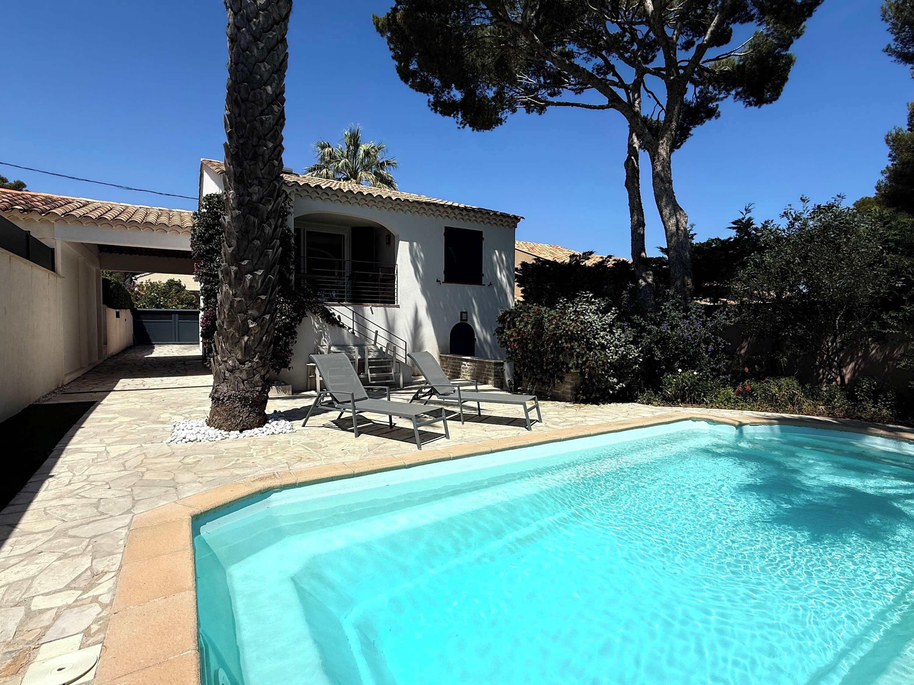 A swimming pool with lounge chairs, a stone pathway, and a building with a tiled roof.