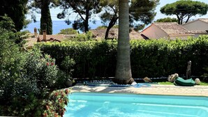 En swimmingpool omgivet af frodig vegetation med udsigt til havet.