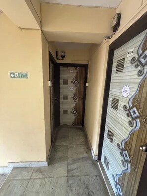 Un couloir étroit, avec un panneau indiquant la sortie de secours, une porte portant le numéro 402 et un sol carrelé.