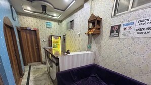 Ein Zimmer mit einem violetten Sofa, einem kleinen Tisch, einer Theke mit einem Coca-Cola Kühlschrank, einem Fenster und einer Wand mit einer Pinnwand.