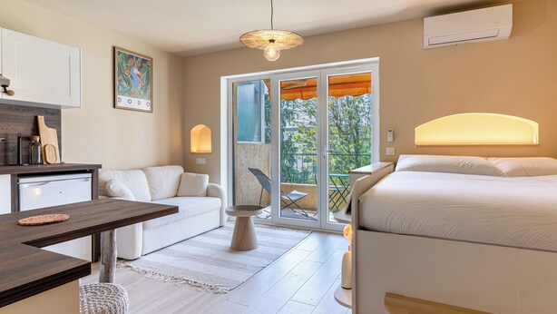 A modern bedroom with a bed, a desk, and a chair. There is a balcony with a view of trees and buildings. - Newly studio apartment in a quiet residence (Mandelieu-la-Napoule)