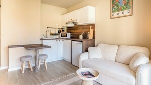 A compact living space with a kitchenette, a sofa, a small dining table with stools, and a magazine on a side table. - Newly studio apartment in a quiet residence (Mandelieu-la-Napoule)