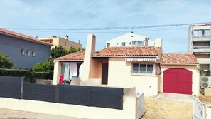 Ein zweistöckiges Haus mit roter Garagentür, einem kleinen Anbau und einem Ziegeldach.