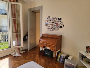 A room with a wooden herringbone floor, a white bed, a wooden desk, a wall of photos, and a door leading to a balcony. - South Balcony Apt - Champs-Élysées (Paris)