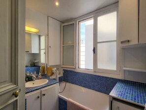 A bathroom with a bathtub, a sink, a mirror, and a window. - South Balcony Apt - Champs-Élysées (Paris)