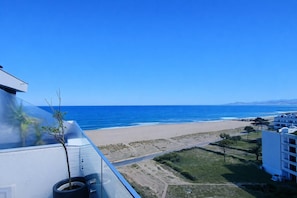 Eine Küstenansicht bei klarem Himmel, ein Strand und ein Gebäude mit Balkon mit Blick auf den Ozean.