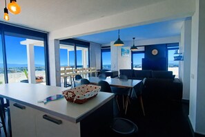 A modern kitchen with a large island, dining area with tables and chairs, and large windows offering a view of the sea. - apartment with terrace in Saint-Cyprien (Saint-Cyprien)