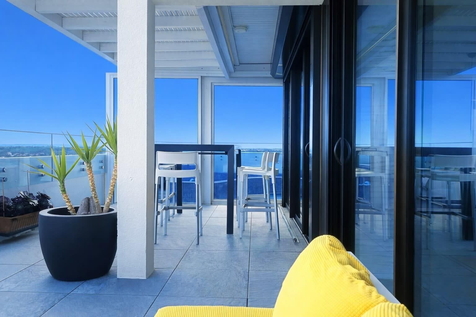 A balcony with a yellow cushion, potted plants, and a view of the sea.