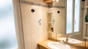 Un bany amb rajoles blanques, un lavabo de fusta, un mirall i una finestra.