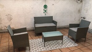 Zona de pati amb mobles de vimet, incloent dues cadires i un sofà, una taula petita i una catifes amb dibuixos sobre terra de rajola.