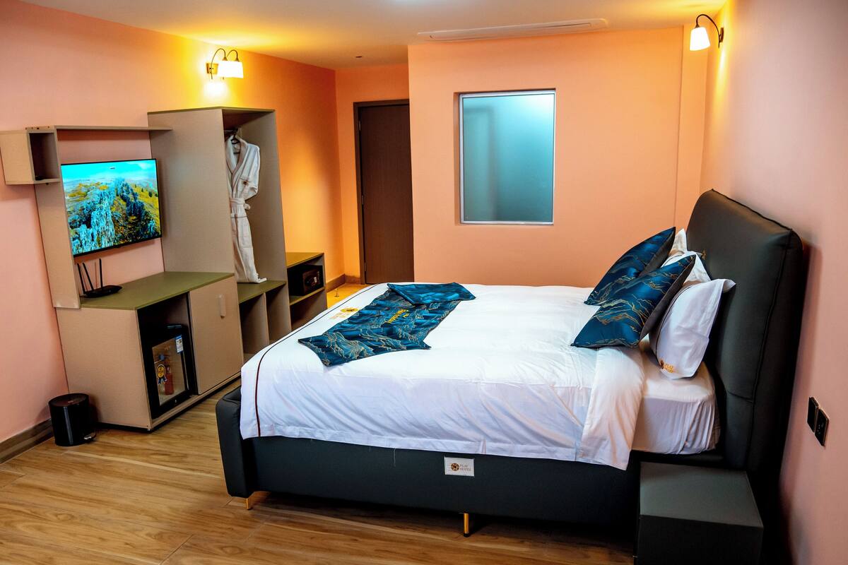 A hotel room with a bed, a TV, a robe, and a small desk with a computer.