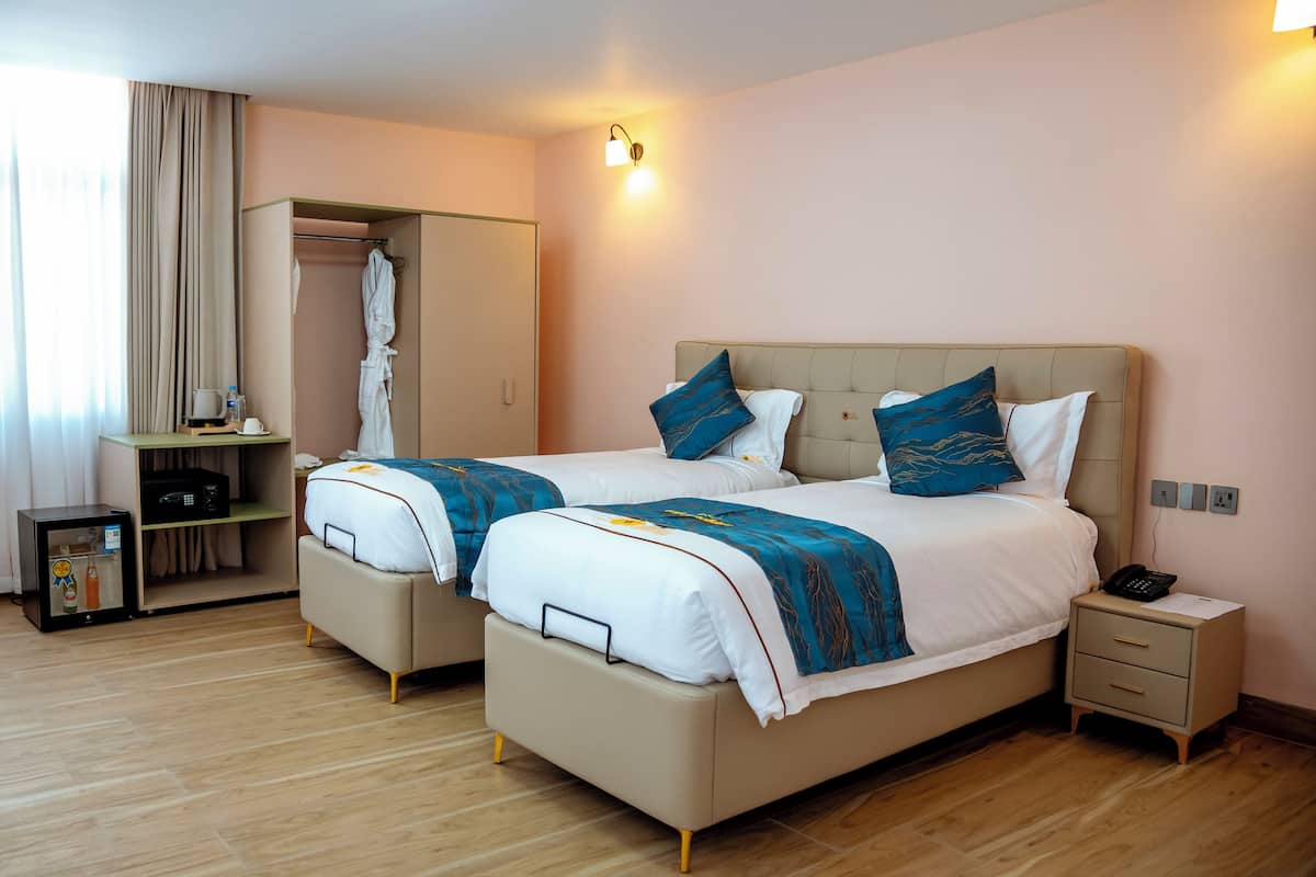 A hotel room with two beds, a wardrobe, a bedside table with a phone, and a small cabinet.