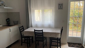 A small kitchen with a dining table and chairs, a window with curtains, a door with a doormat, and a sign indicating WiFi availability.