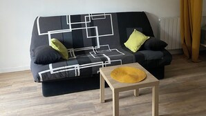 A living room with a black sofa, a framed picture on the wall, a small wooden table, and a yellow curtain.